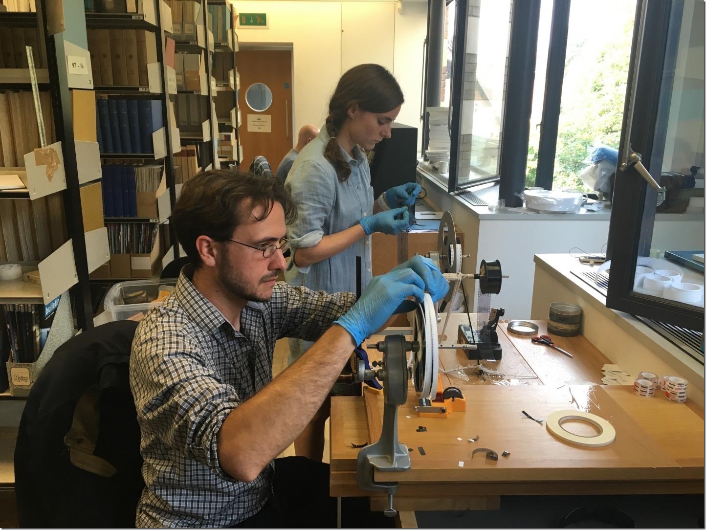 Professor Dustin Schroeder (foreground) and art historian Jessica Daniel splice 50-year-old film containing radar measurements of Antarctica into a reel in preparation for digital scanning at the Scott Polar Research Institute in the UK. Credit Courtesy of Dustin Schroeder